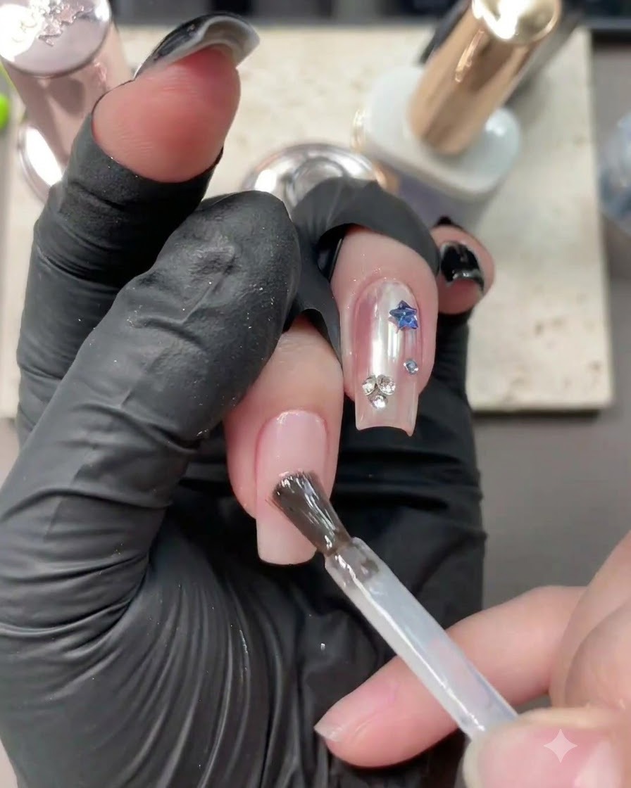 Un pincel aplicando gel base transparente sobre una uña nude neutra que ya tiene un diseño.