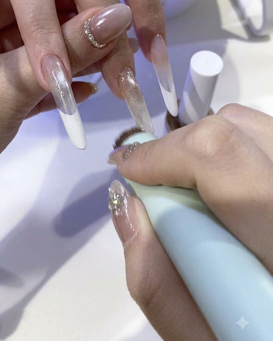 Un pincel aplicando una mezcla brillante de gel con polvo de hadas en la punta de una uña extendida.