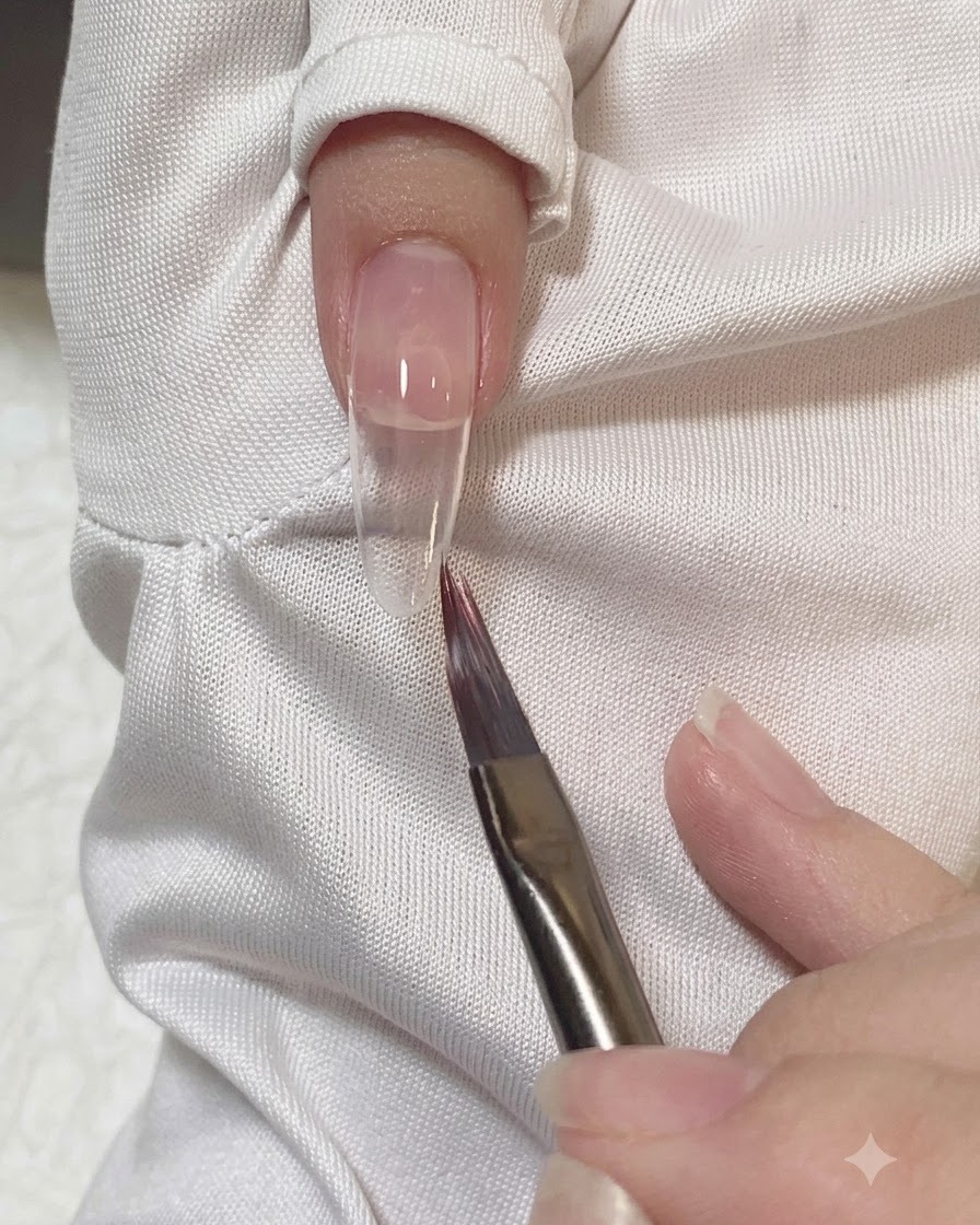 Un pincel plano suavizando y difuminando los bordes de gel rosa sobre la uña.