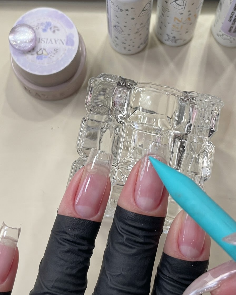 Un pincel azul aplicando una base transparente peel-off en la zona de la cutícula de una uña natural.