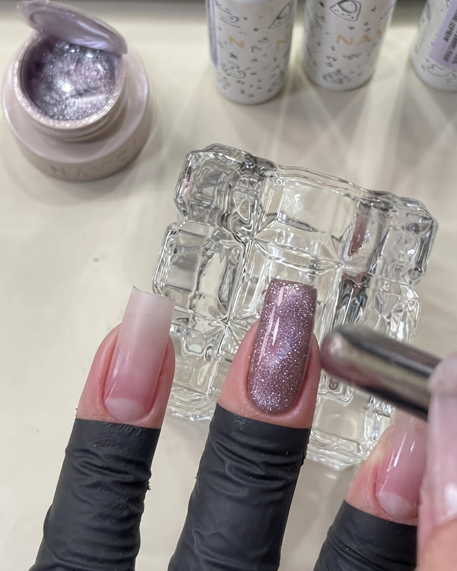 Una herramienta magnética sostenida cerca de una uña con manicura para moldear el gel cat eye brillante en un efecto de cuenta de vidrio luminoso.