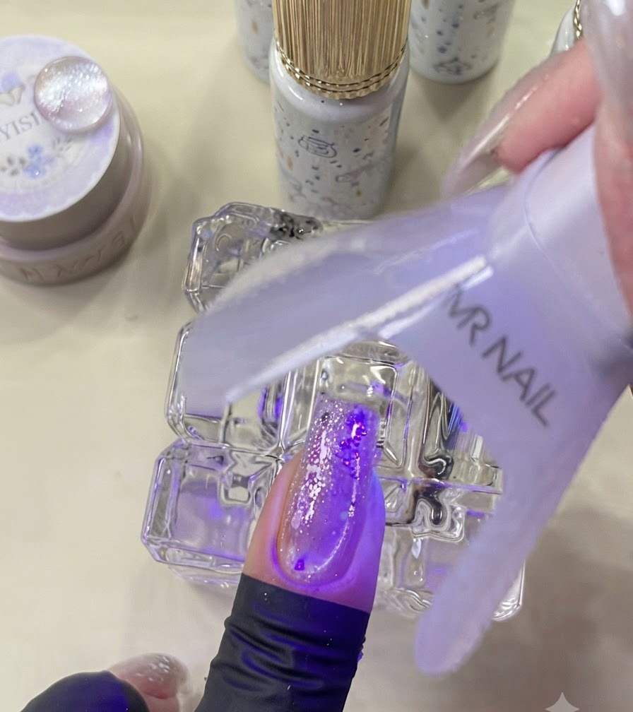 Una mini lámpara UV curando una uña decorada bajo luz púrpura.