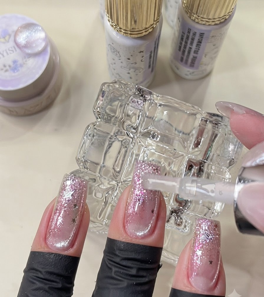 Un pincel aplicando el top coat final en uñas terminadas de estilo galaxia.