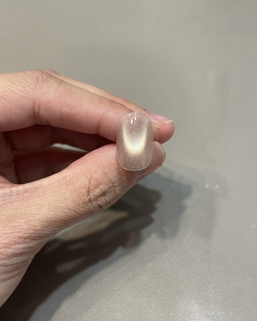 Una sola uña manicurada con un esmalte ojo de gato rosa dorado curado con un reflejo de luz centrado.