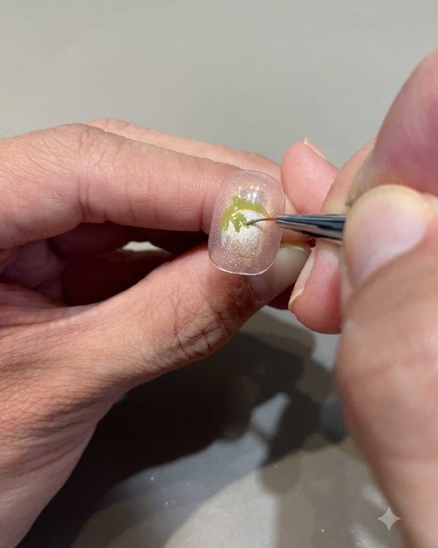 Una vista de cerca de un pincel fino de detalle rellenando meticulosamente con gel verde aguacate para crear hojas de fresa en una uña nude rosada.