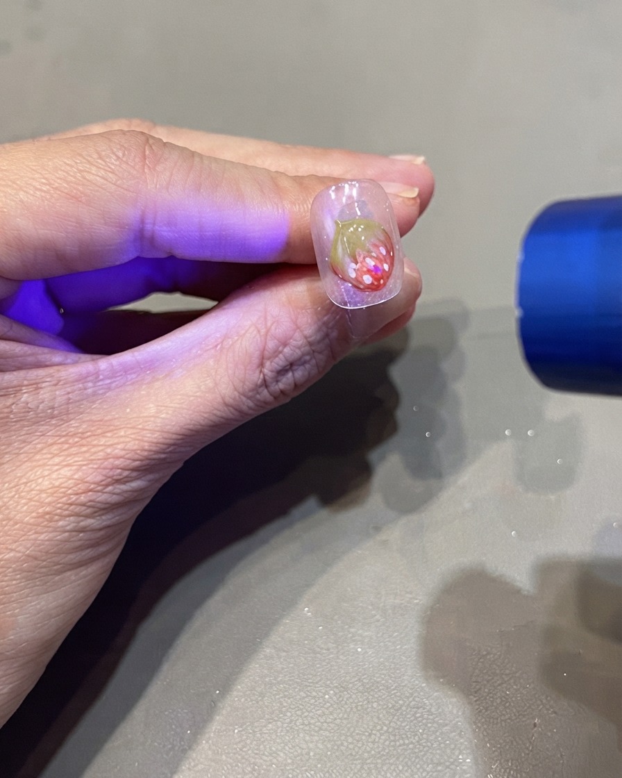 Una linterna UV portátil curando un diseño de uña de fresa 3D.