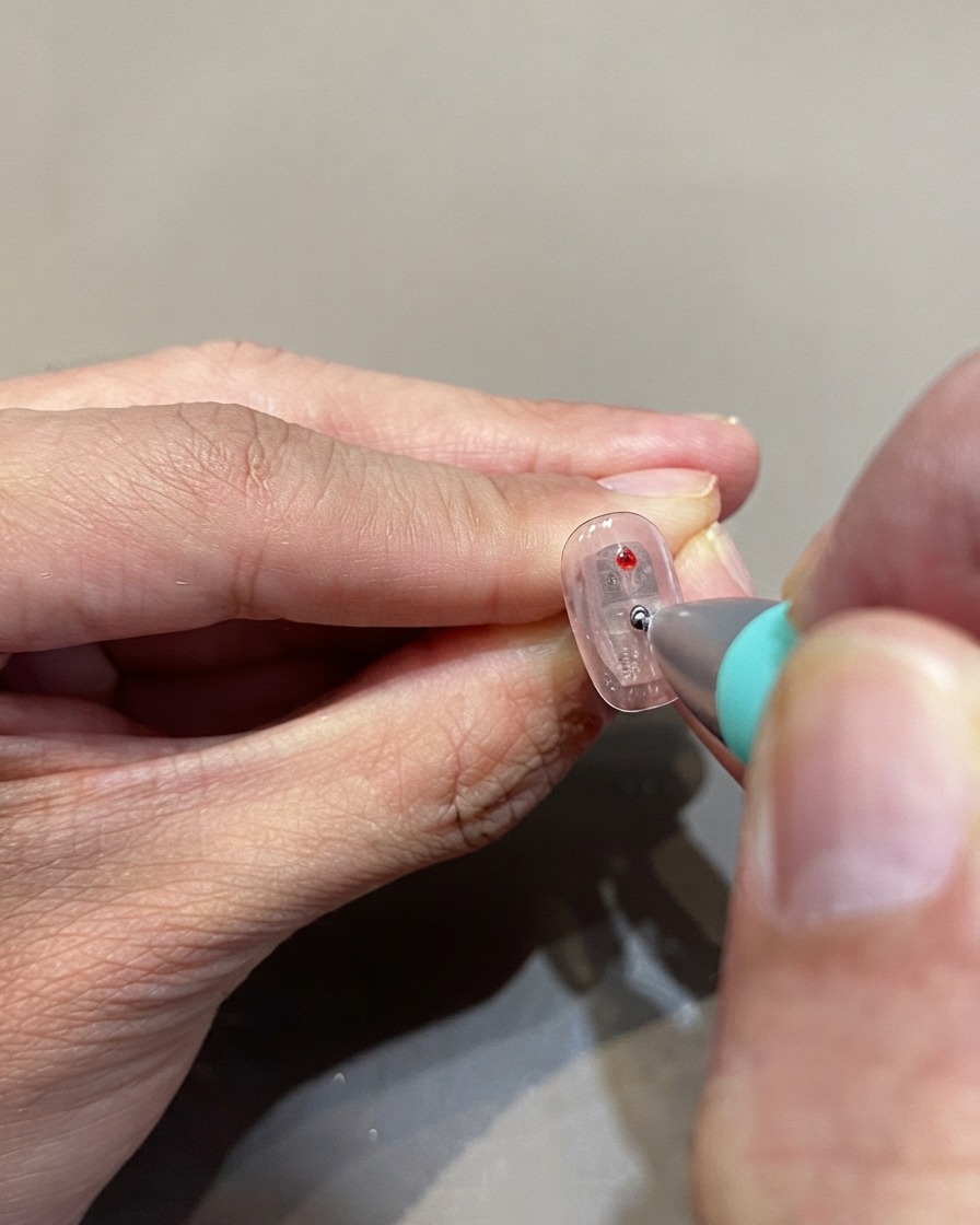 Una herramienta puntera colocando lunares de gel de vidrio rojo en una superficie de uña transparente.