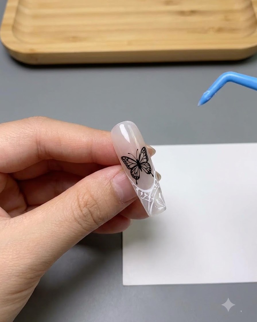 Primer plano de una uña decorada con un detallado patrón de mariposa hueca en color blanco.