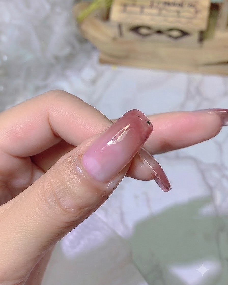 Una pequeña gota de gel adhesivo transparente colocada cerca del borde de la uña con degradado terminada.
