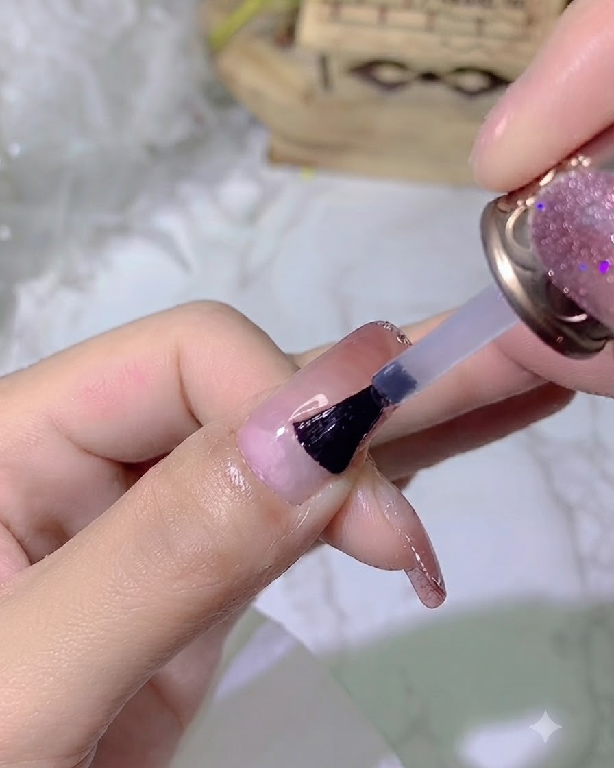 Una brocha aplicando un top coat brillante y transparente sobre una uña con manicura.