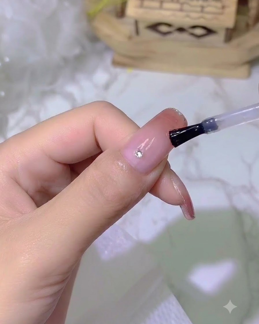 Un pequeño cristal brillante siendo colocado sobre una uña usando una herramienta de detalle.