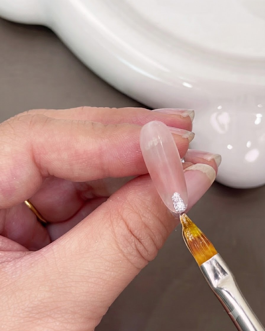 Un pincel fino aplicando gel blanco brillante en la punta de una uña.