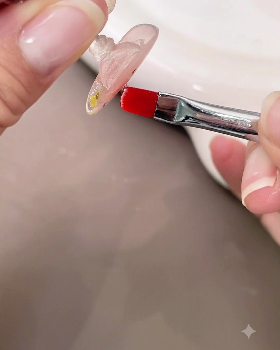 Una mano sosteniendo una uña boca abajo mientras usa un pincel pequeño para verificar el ápice autonivelante del gel de construcción transparente.