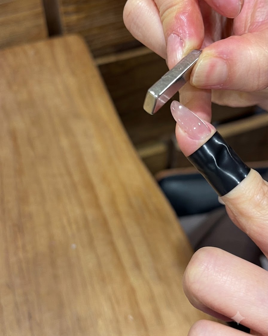 Imán de barra rectangular sostenido verticalmente cerca de una uña pintada con gel brillante para empujar las partículas magnéticas.