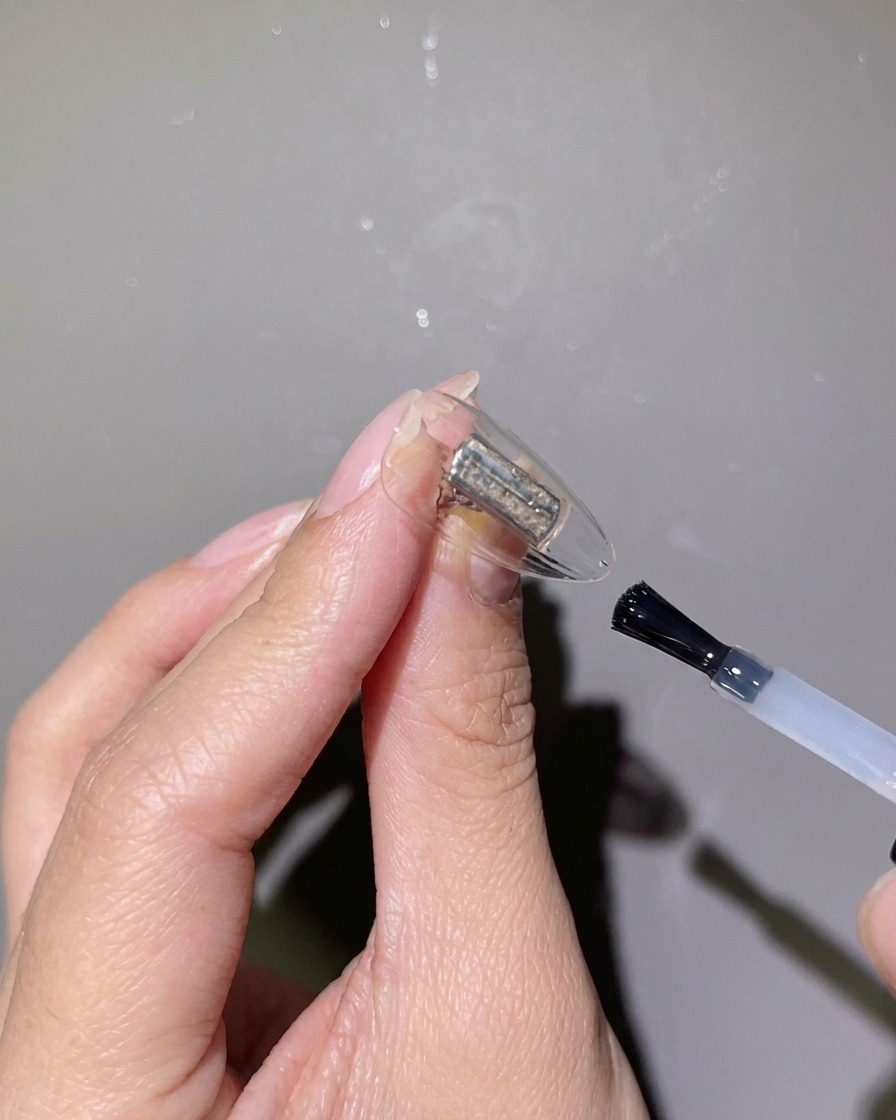 Un primer plano de un pincel de uñas aplicando gel de refuerzo transparente sobre una punta de uña transparente.