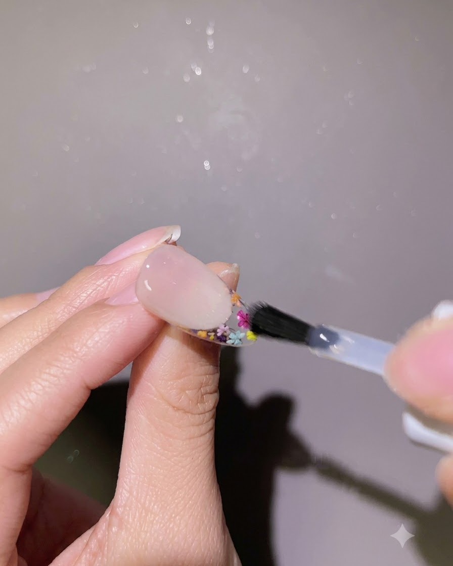 Un pincel aplicando una capa de gel de refuerzo transparente alrededor de los bordes de un diseño de uña completado.