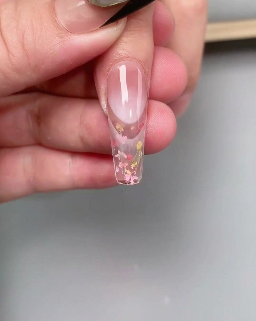 Un pincel liner fino difuminando esmalte de gel rosa en el área de la cutícula de una uña para crear un efecto degradado.