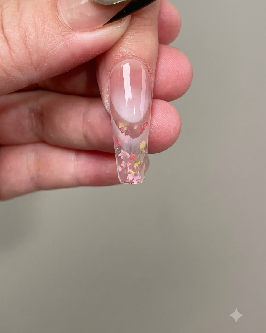 Unas pinzas colocando diminutas flores secas rosas y amarillas sobre el gel de uñas húmedo.