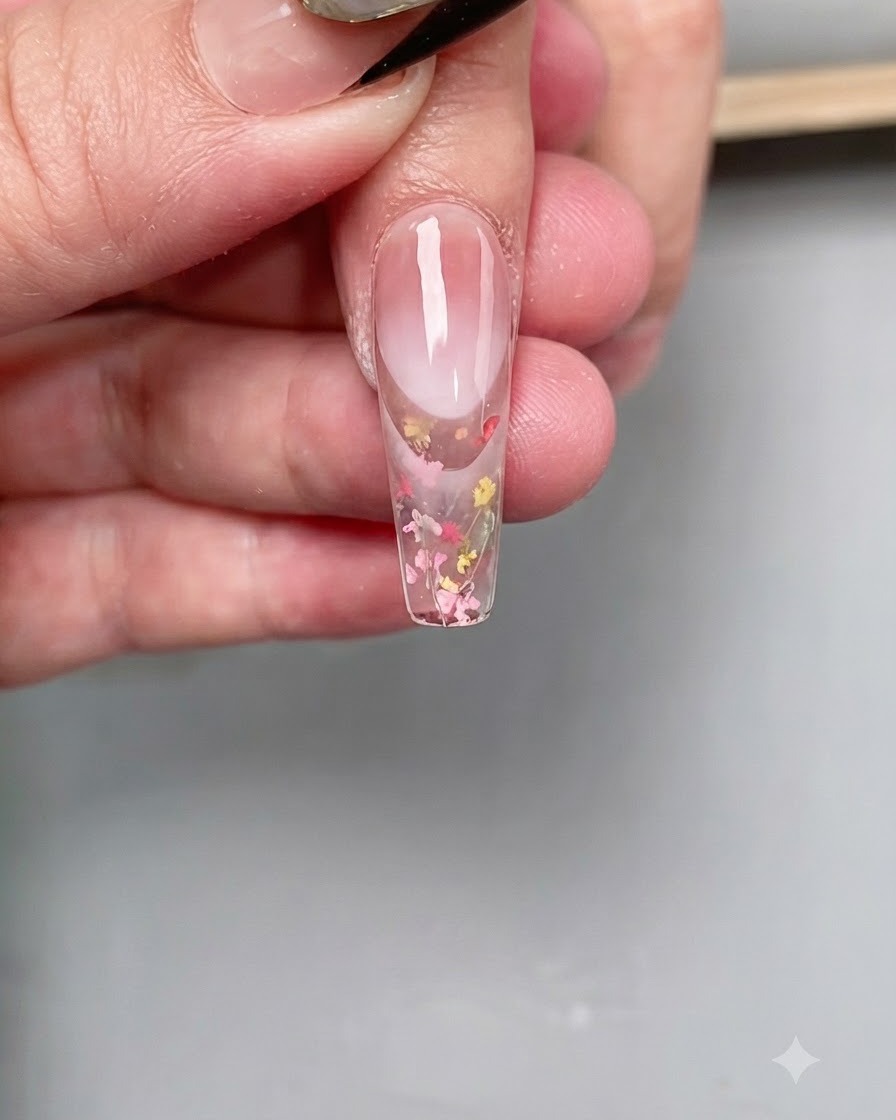 Un pincel fino de nail art aplicando un top coat diamante transparente precisamente sobre la punta de una uña larga en forma de ataúd.