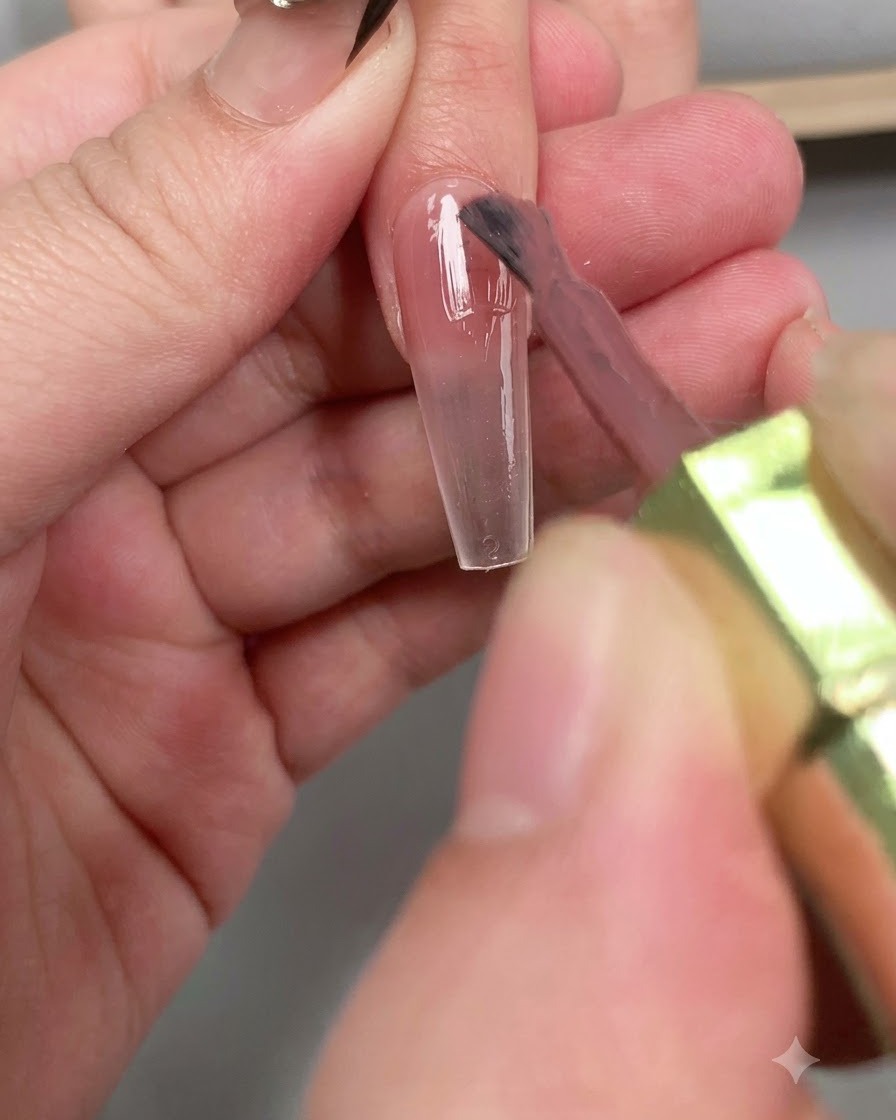 Un pincel aplicando una capa brillante de top coat diamante en toda la longitud de la uña.