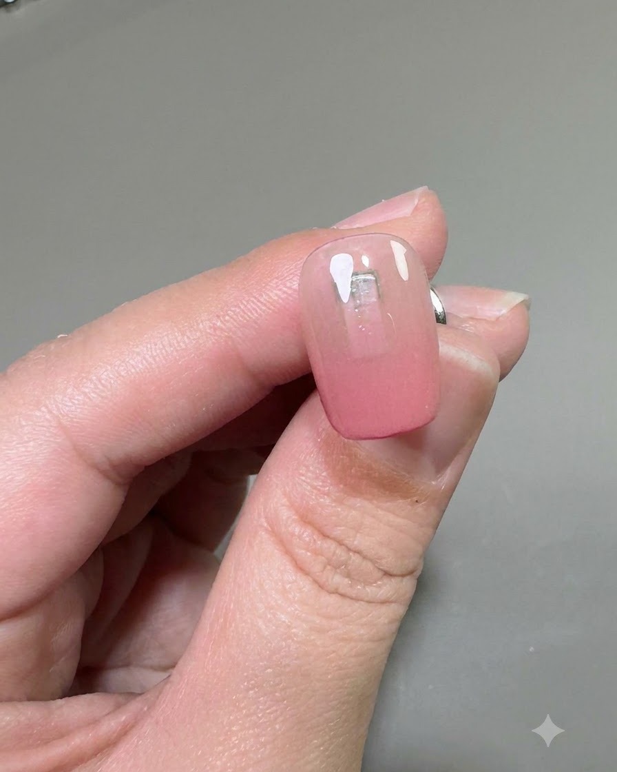 Primer plano de una uña que muestra una capa transparente de gel de refuerzo aplicada sobre la base degradada rosa.