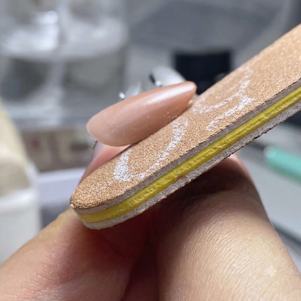 Un taco pulidor de uñas dando forma y suavizando los tres lados de una uña de gel terminada.