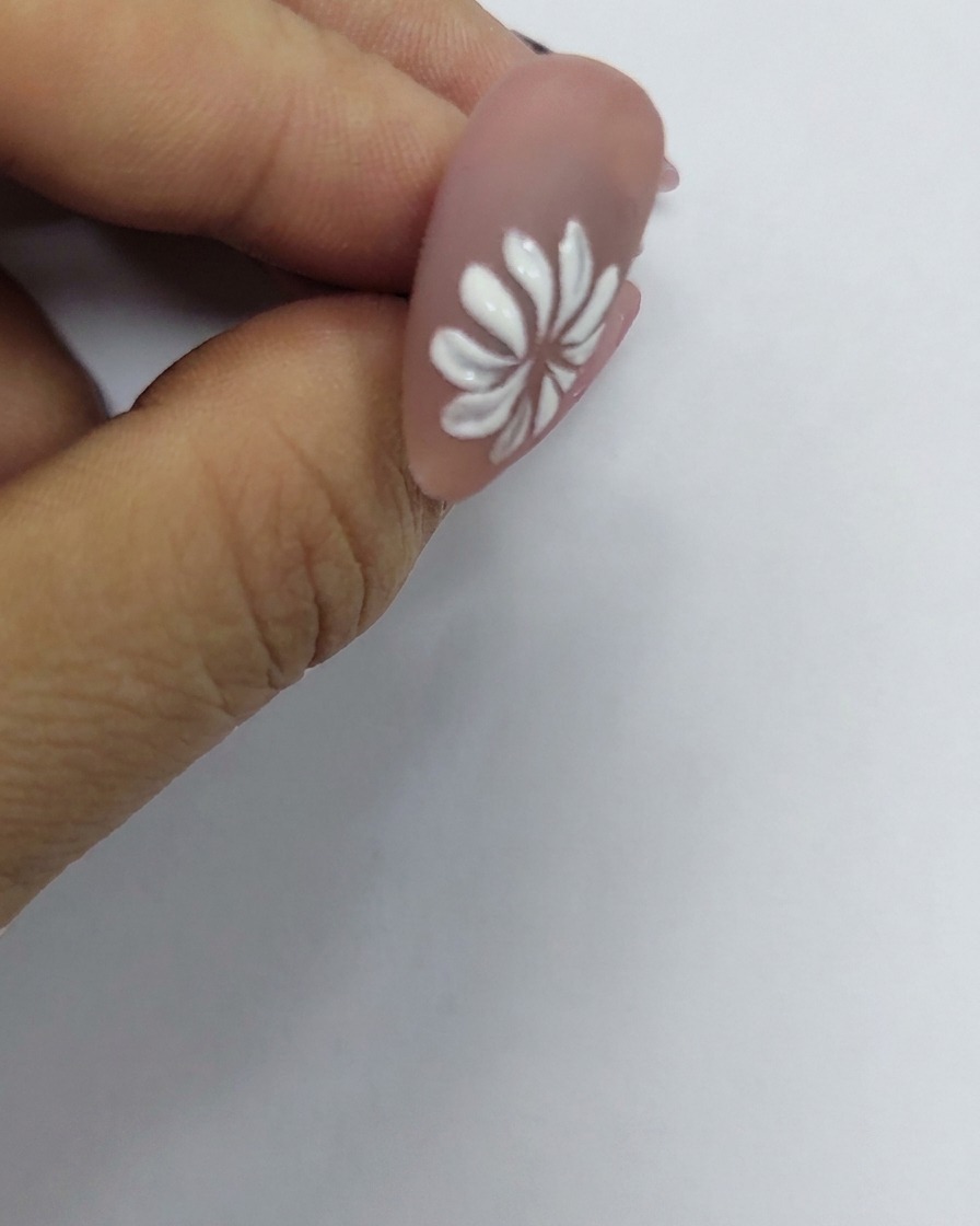 Una flor de margarita blanca pintada en una uña con un diminuto punto amarillo colocado precisamente en su centro.
