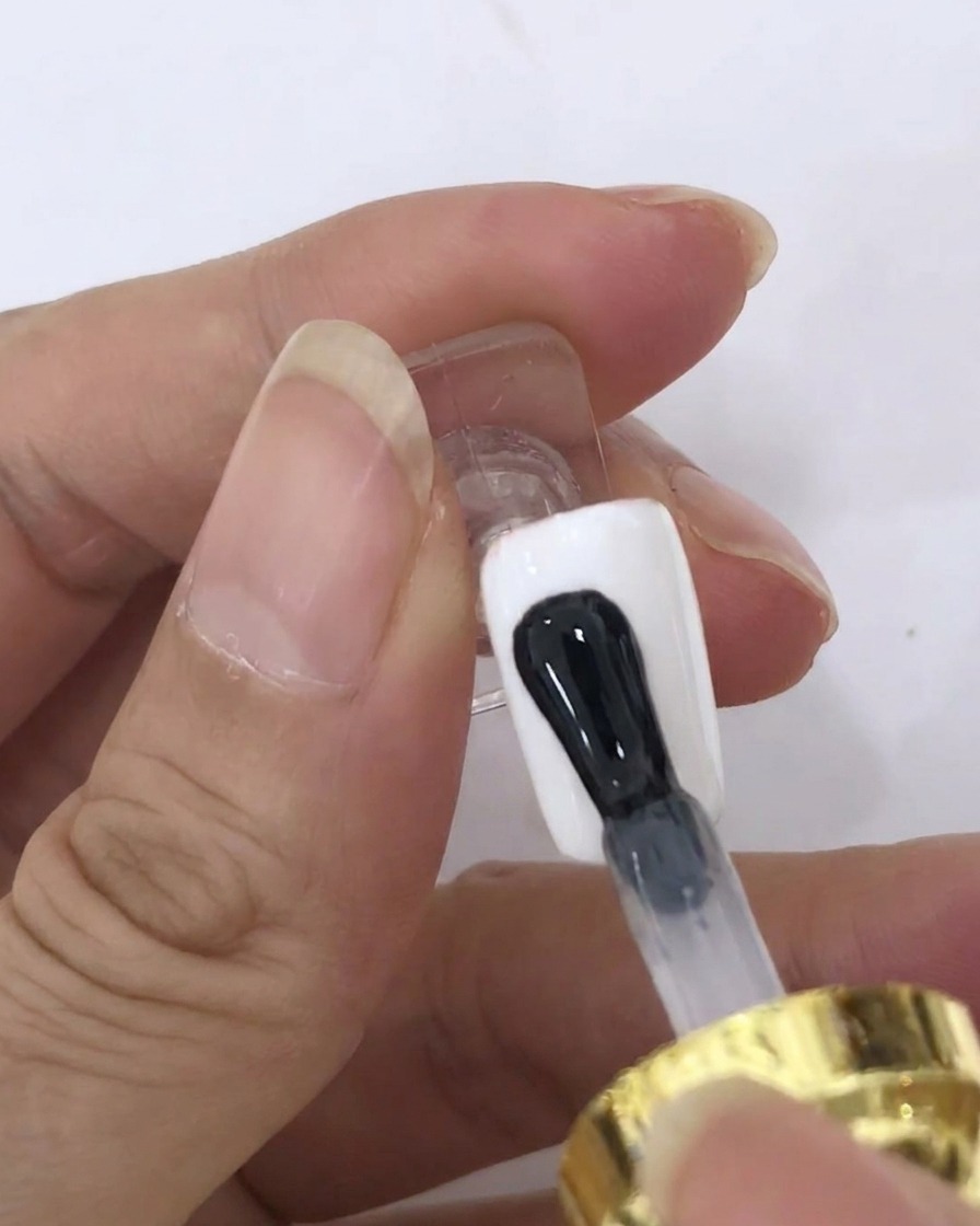 Un pincel aplicando una capa transparente de blooming gel sobre la superficie de una uña pintada de blanco.