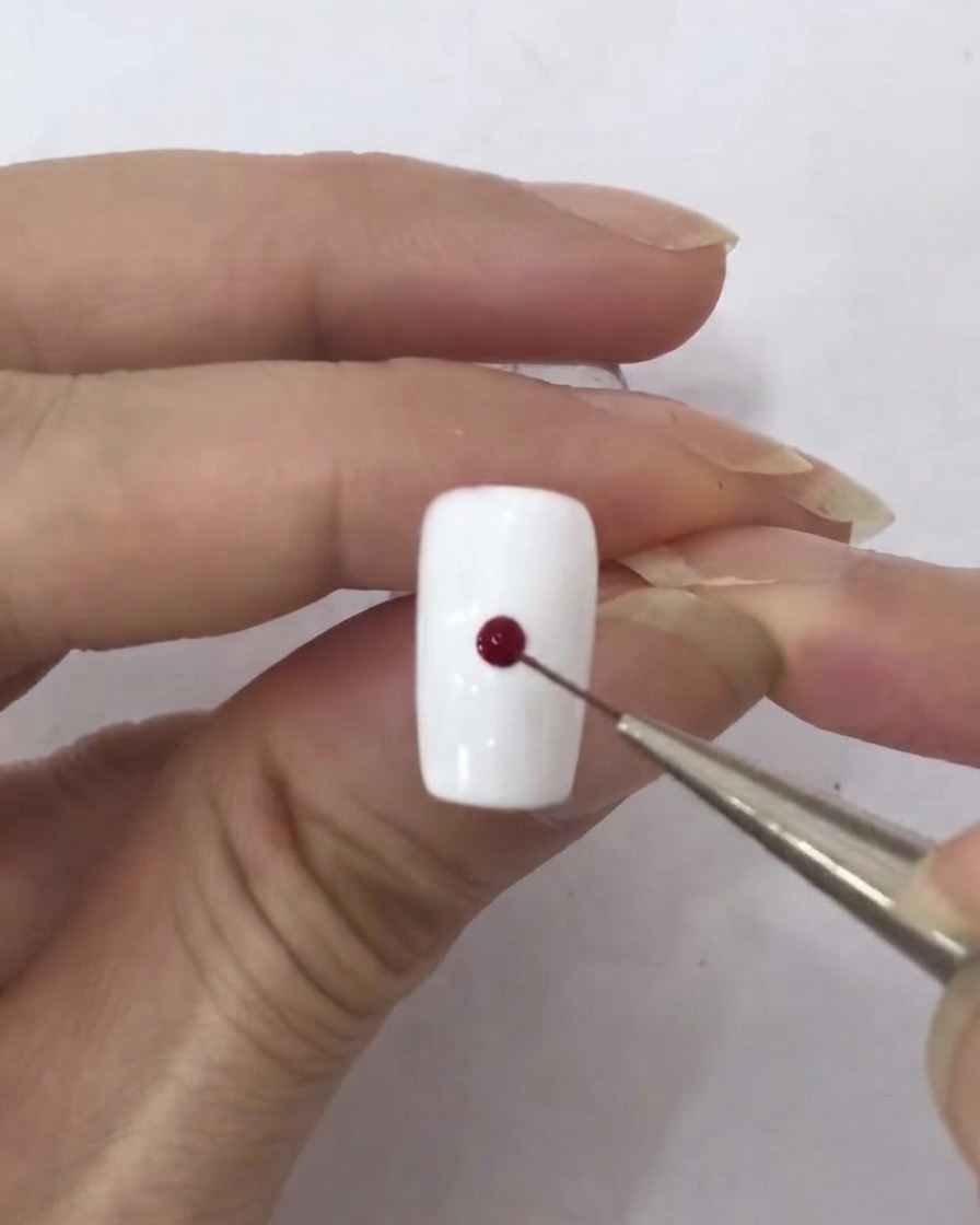 Un pincel delineador fino tomando una pequeña gota de esmalte en gel rojo oscuro.