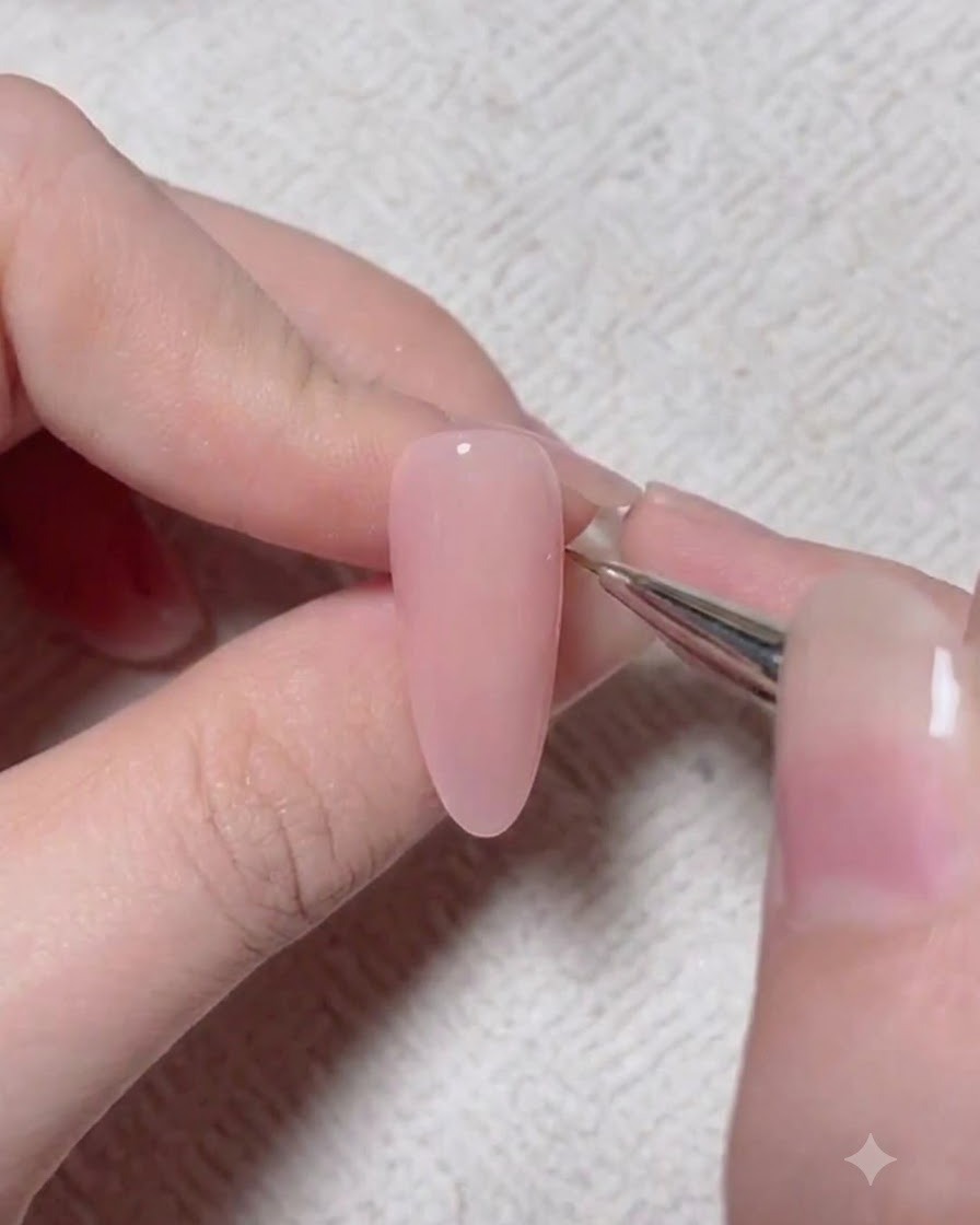 Un pincel de detalle aplica un pigmento de acento más oscuro sobre la superficie de una uña de gel rosa.