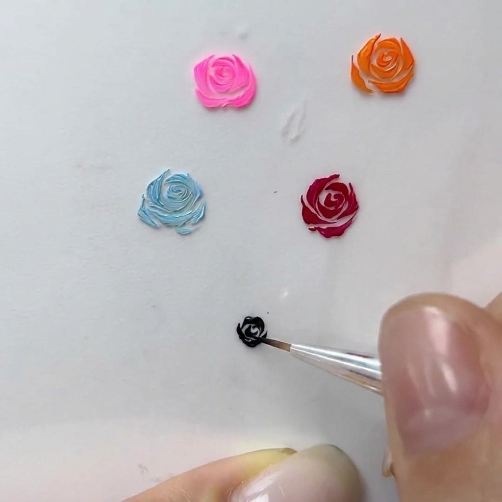 Una vista macro de un artista de uñas añadiendo trazos curvos finos al borde de una rosa de gel negra.