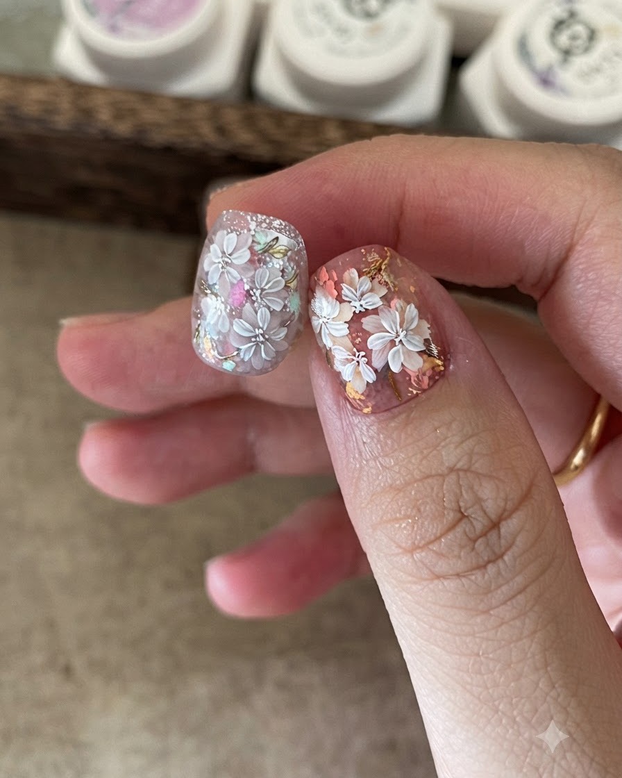 Un primer plano de una artista de uñas usando una pequeña esponja para aplicar gel de color en el centro del diseño floral blanco.