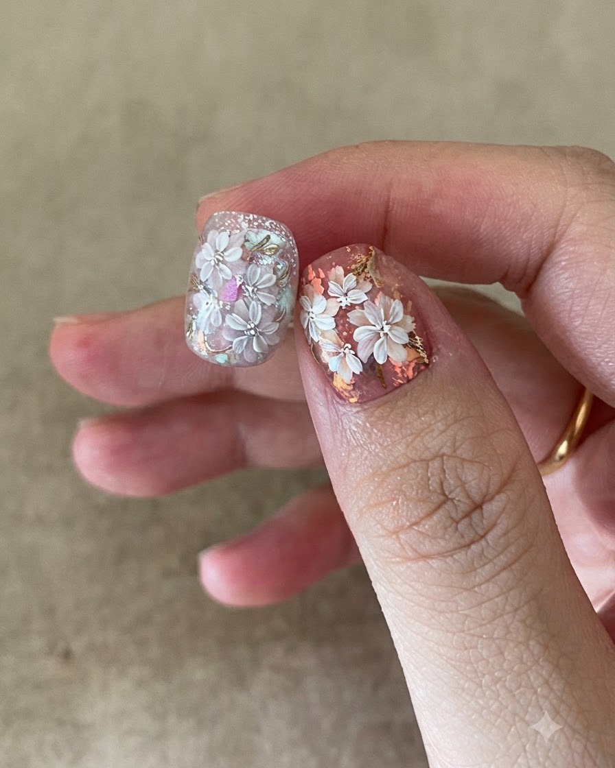 Un pincel de uñas aplicando una capa superior transparente sobre un diseño de arte en uñas floral y con papel dorado.