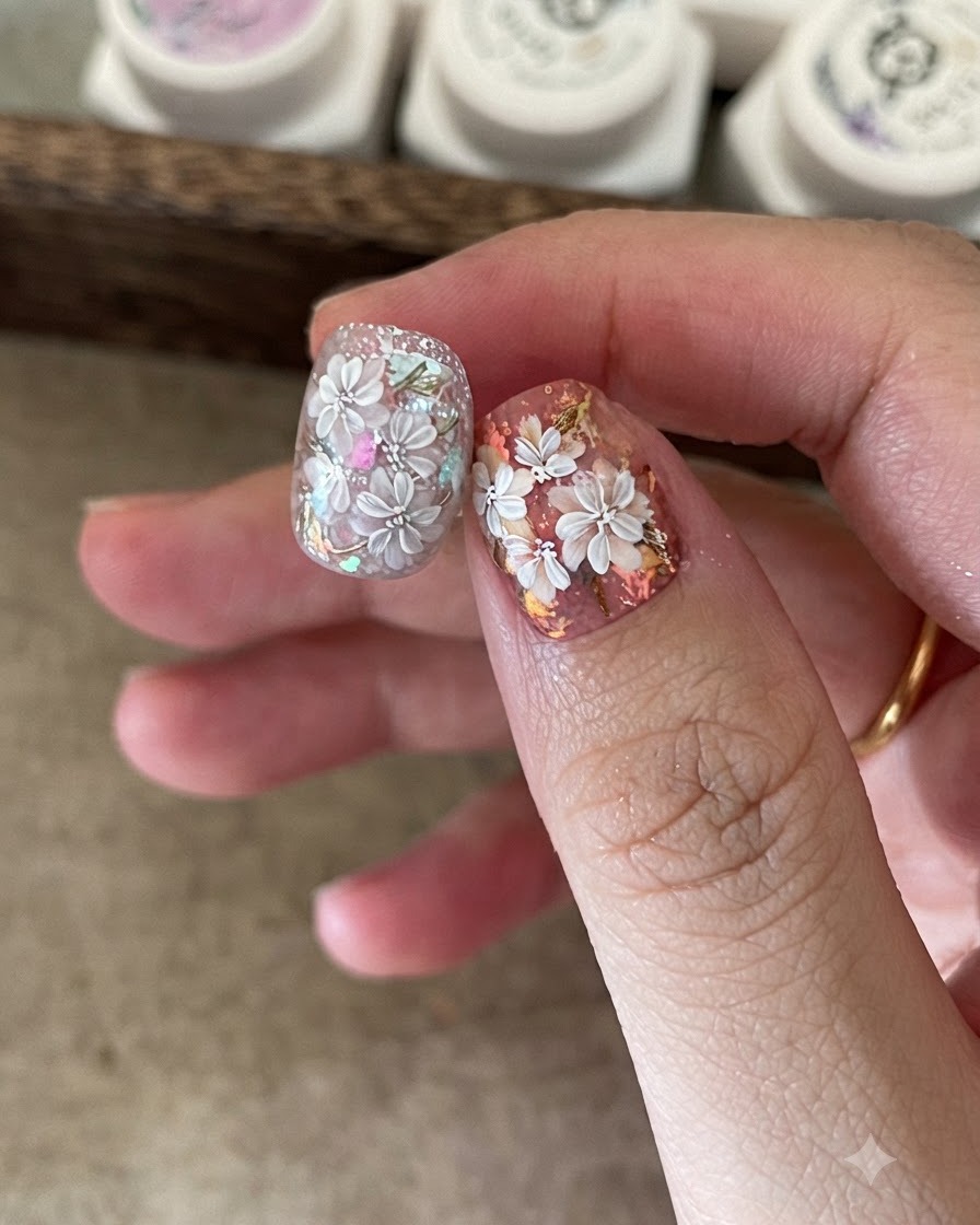 Un pincel fino para nail art agregando pétalos blancos detallados sobre un diseño floral previamente pintado.
