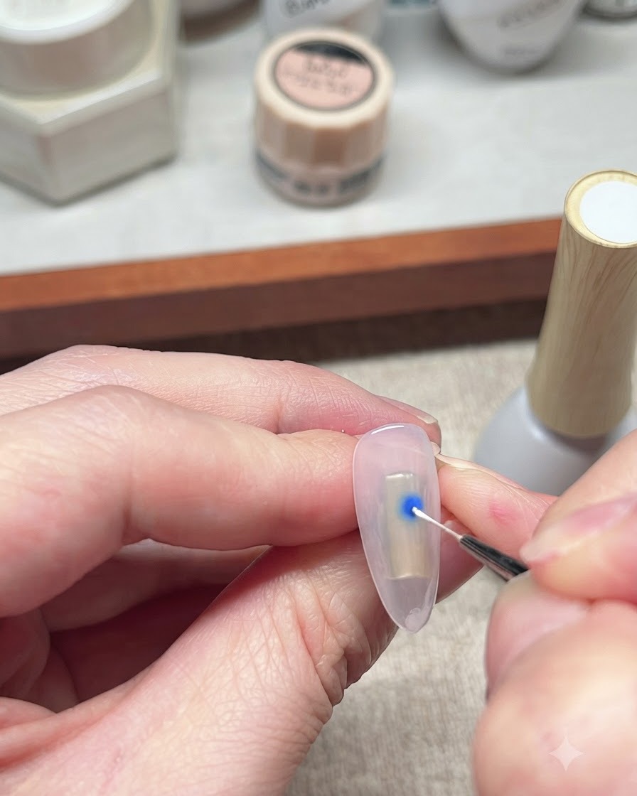 Un pincel delineador fino interactuando con un punto azul de esmalte en gel sobre una uña para iniciar el efecto de floración.