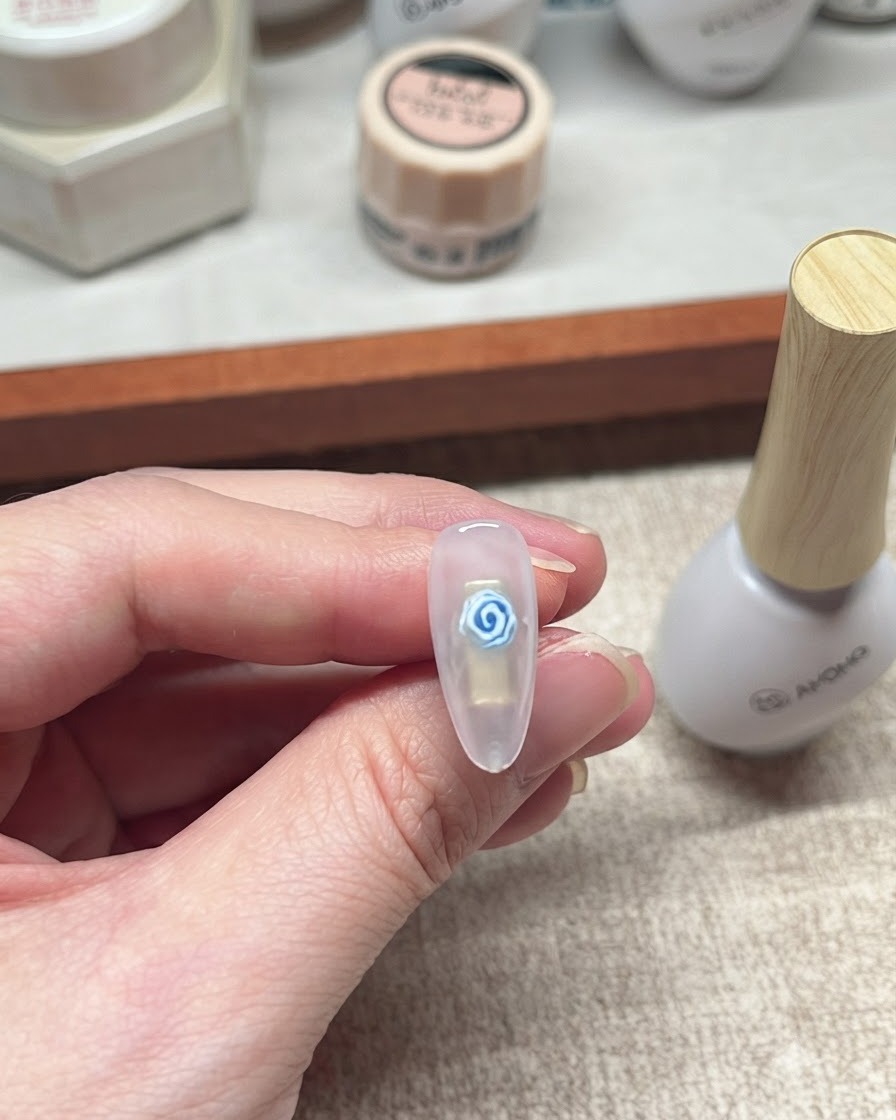 Primer plano de un diseño de uñas de gel con rosa azul terminado, descansando junto a una botella blanca de producto para uñas.