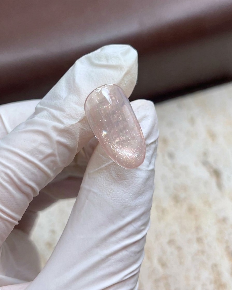 Una mano con guantes sosteniendo una varita magnética sobre una uña de gel ojo de gato brillante para crear un efecto de perla.