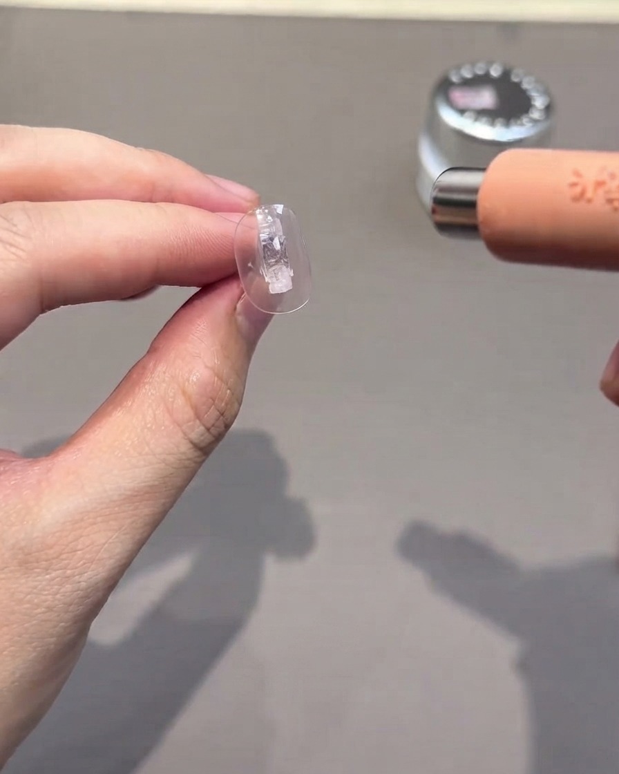 Una punta de uña transparente curándose bajo una lámpara UV/LED pequeña y portátil.