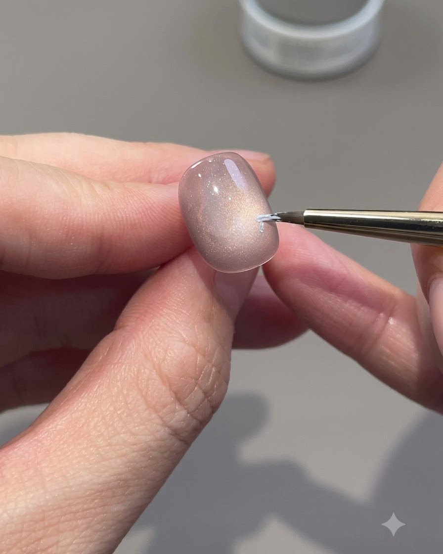 Un pincel delineador fino dibujando contornos de rosas blancas en una uña de gel cat-eye.