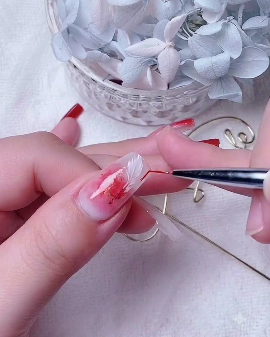 Primer plano de una artista de uñas utilizando un pincel de detalle delgado para difuminar gel rojo en una uña con base blanca lechosa.