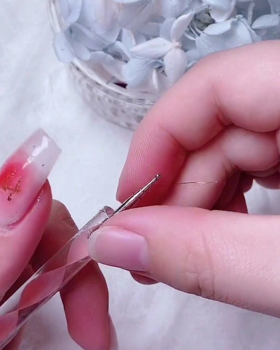 Pinzas finas colocando una pequeña e intrincada rosa de alambre dorado en el centro de una uña decorada.