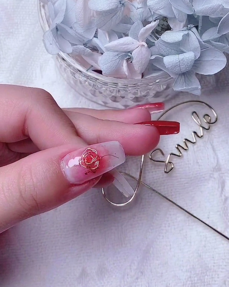 Primer plano de una uña de pulgar decorada con una rosa de alambre dorado y pequeños alambres de acento a lo largo del borde.