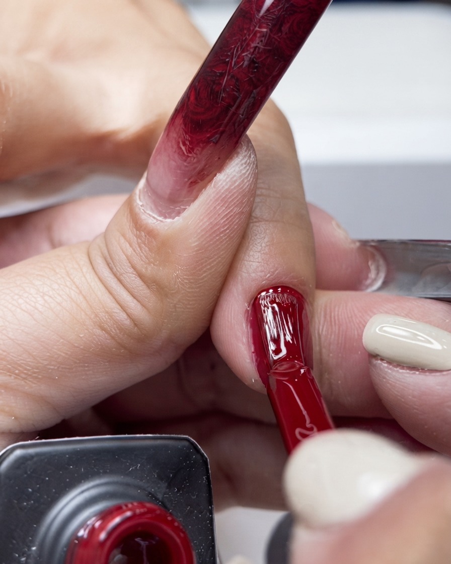 Un pincel aplicando esmalte en gel rojo vibrante por el centro de una uña.