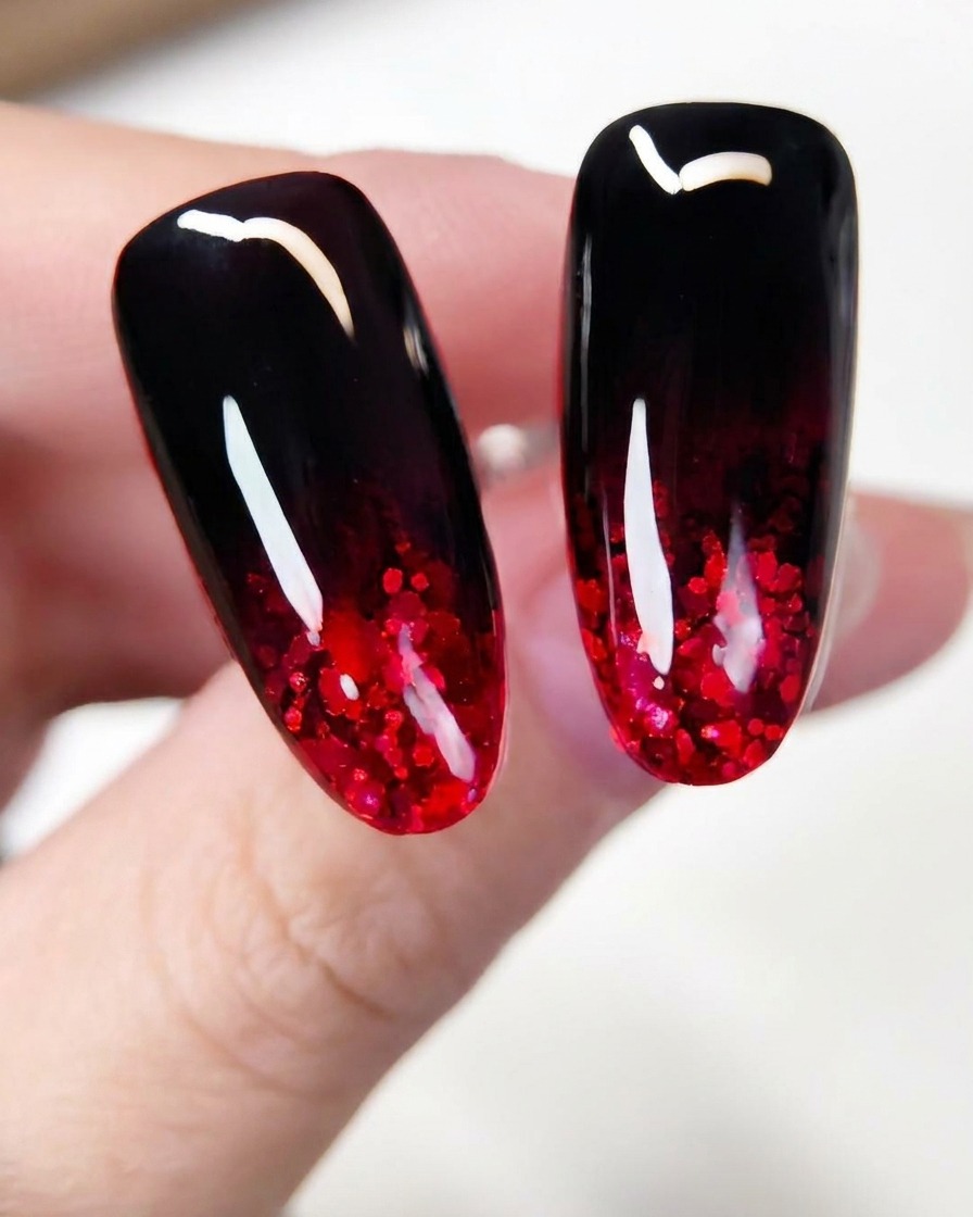 Un primer plano de un pincel extendiendo escamas brillantes de purpurina roja por la sección inferior de una extensión de uña pintada de oscuro.