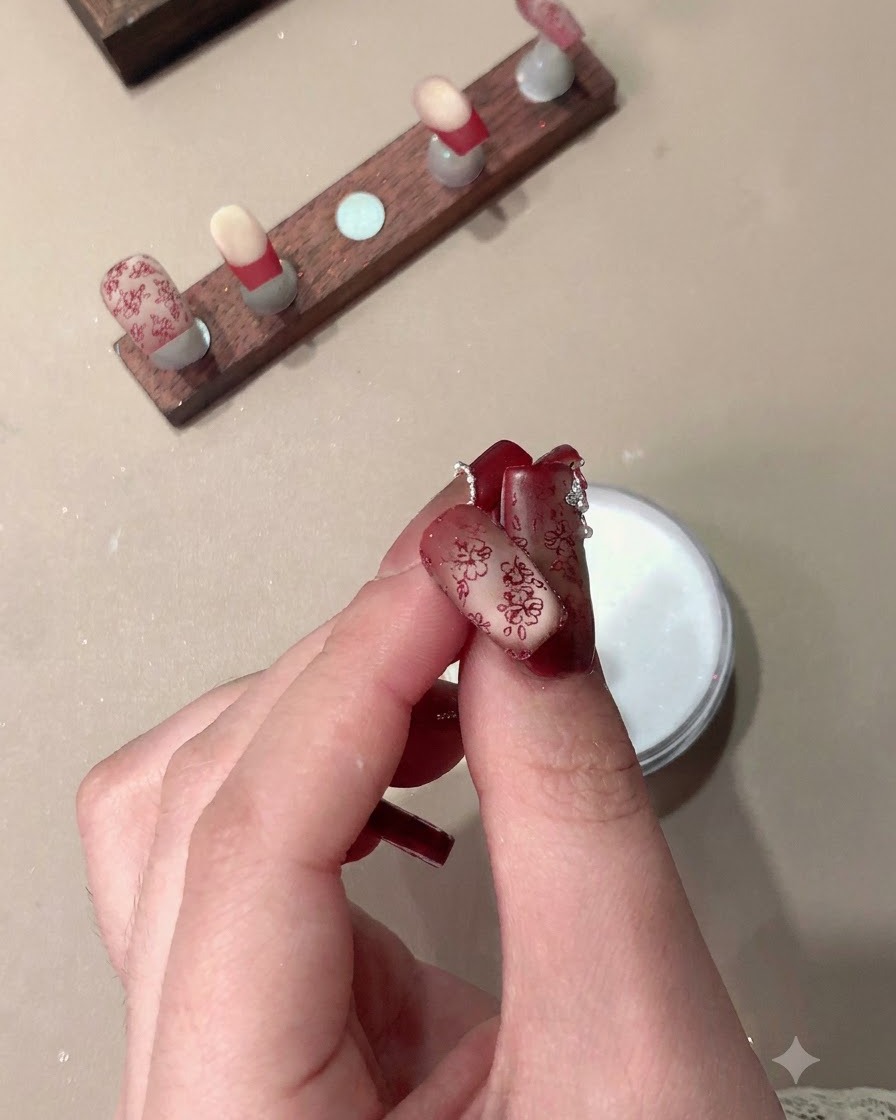 Una mano sosteniendo uñas postizas terminadas que presentan patrones rojos estampados y puntas francesas.