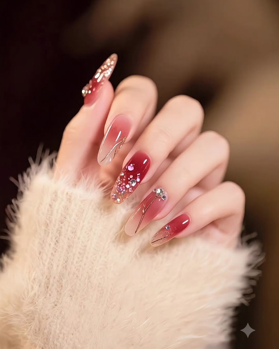 Una mano que muestra uñas largas cuadradas con una transición suave desde el nude hasta el burdeos profundo, decoradas con escamas doradas.