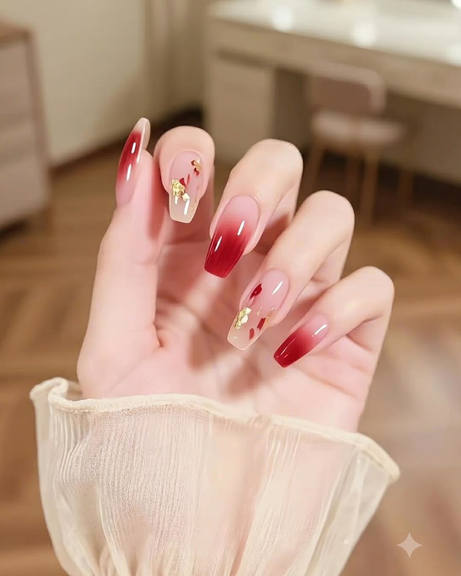 Un primer plano de una mano con una uña de acento con pinceladas multicolores abstractas y brillos dorados junto a uñas ombre burdeos.