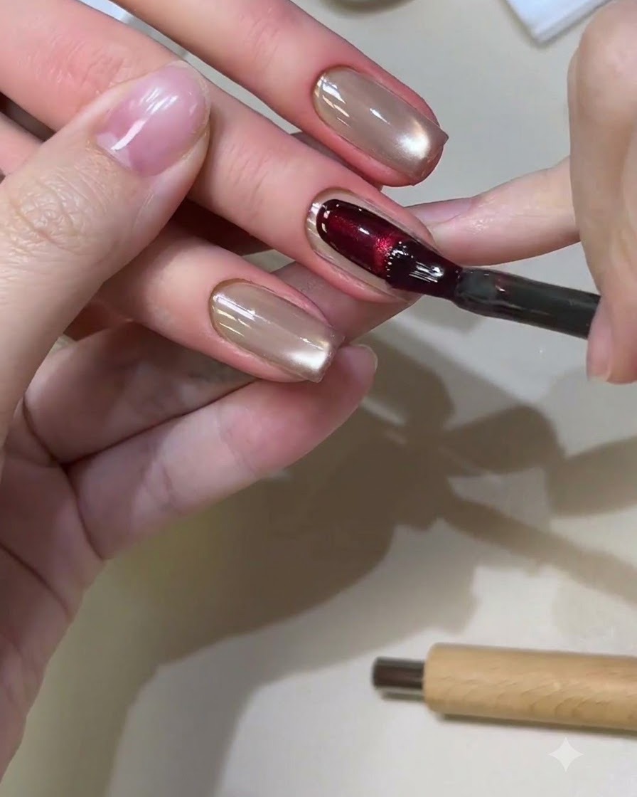 Un pincel de uñas aplicando un gel cat-eye rojo intenso sobre una uña de forma cuadrada.