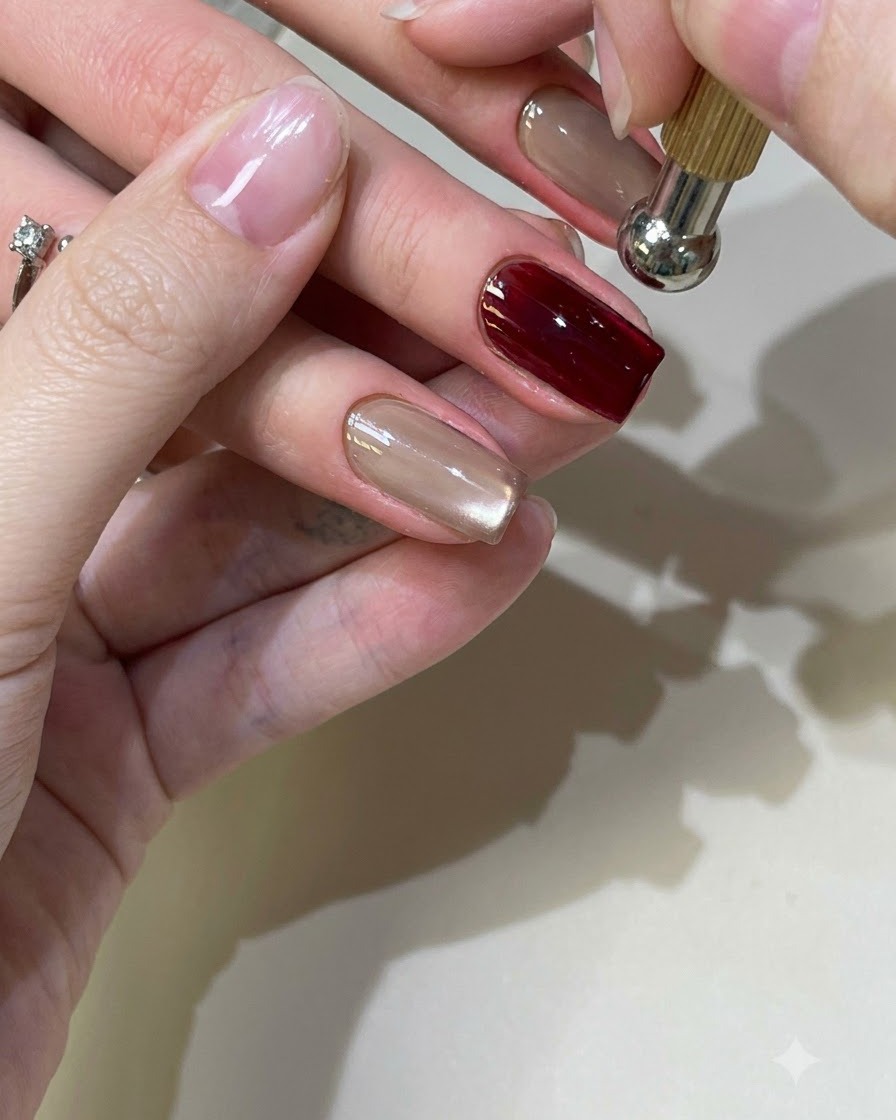 Una herramienta magnética esférica flotando sobre una uña con gel cat-eye rojo para dar forma al reflejo de luz.