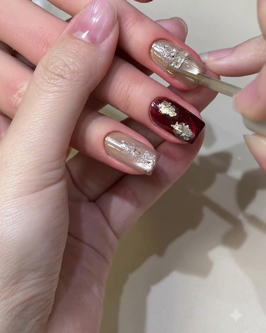 Un pincel fino aplicando meticulosamente detalles de líquido metálico dorado sobre un diseño de uñas texturizado y brillante.